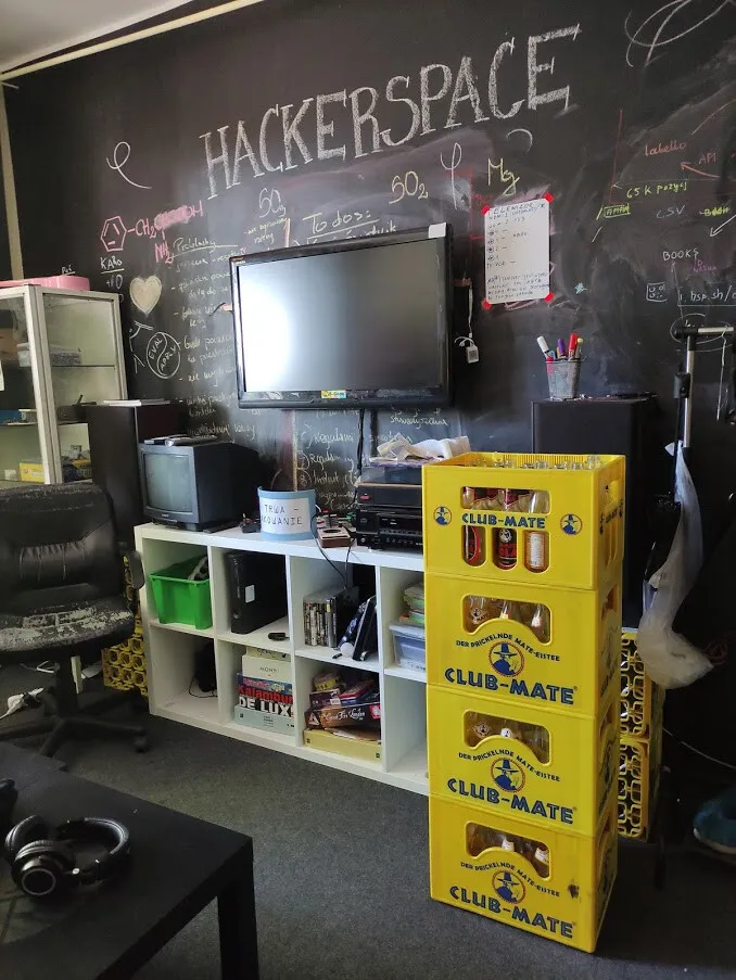 Kącik w hackerspace'ie z tablicą kredową, telewizorem i skrzynkami napojów